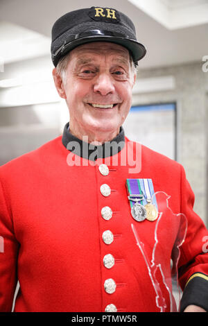 Victoria Station, London, 10. Okt 2018. Chelsea Rentner Tony, die erst 80, in seiner traditionellen scharlachroten Mantel. Die Veteranen sammeln Spenden in zwölf Londoner U-Bahn-Stationen, heute im Namen der Nächstenliebe "erinnert". Eröffnungs-Projekt der Nächstenliebe", es aber nicht Es' hat das Ziel, zum Gedenken an jene, die in der WK 1 starb, die Jungen zu erziehen und die heutigen Veteranen leiden von der mentalen und körperlichen Wunden der Service während der Hundertjahrfeier 2018 heilen. Credit: Imageplotter Nachrichten und Sport/Alamy leben Nachrichten Stockfoto