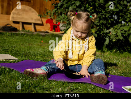 Wenig Trauriges Mädchen sitzt auf einem Gras und schaut auf das Essen Stockfoto