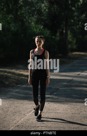 Athletische Frau in Sportkleidung zu Fuß auf dem Weg in den Park Stockfoto