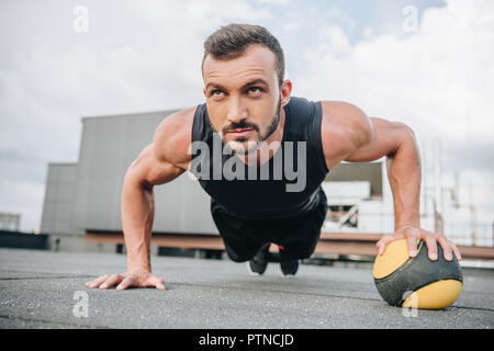 Schöne muskulöse Sportler tun Push-ups mit Medizinball auf dem Dach Stockfoto