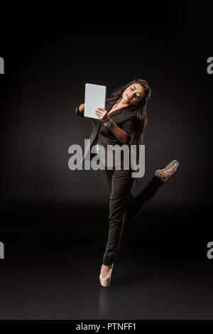 Junge Geschäftsfrau in Anzug und Ballett Schuhe mit Tablet auf schwarzem Hintergrund Stockfoto