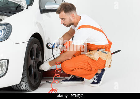 Stattliche Automechaniker Aufpumpen von Reifen und die Kontrolle der mit Überdruck auf Weiß Stockfoto