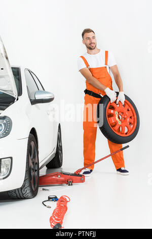 Automechaniker in Orange einheitliche Durchführung von PKW-Reifen auf Weiß Stockfoto