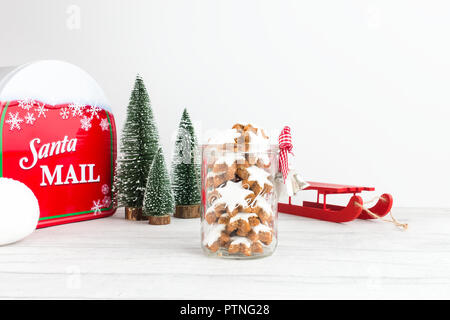 Weihnachtsplätzchen, Deutschen, Zimtsterne Zimtsterne in einem Glas mit Weihnachtsdekoration, einen Schlitten, Tannen, ein Santa Mailbox und ein Schneeball. Stockfoto