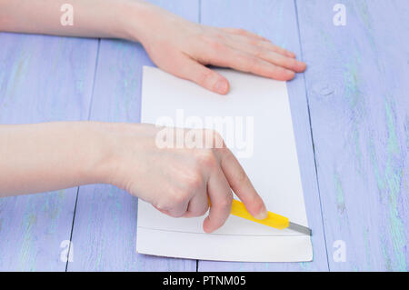 Ein Mädchen Schnitte Karton mit einer feststehenden Messer auf einem violetten Hintergrund aus Holz. Close-up. Stockfoto