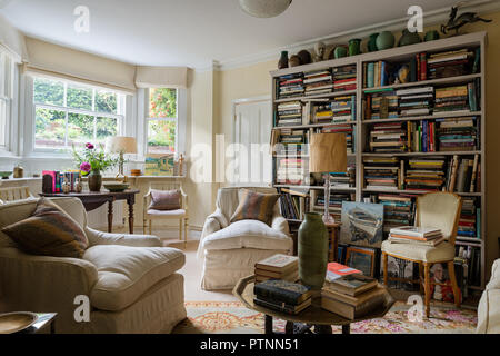 Custom made Bücherschrank für die Bibliothek mit Büchern über Kunst und Design. Ein Howard stil Sessel in Creme Bettwäsche gepolstert Stockfoto