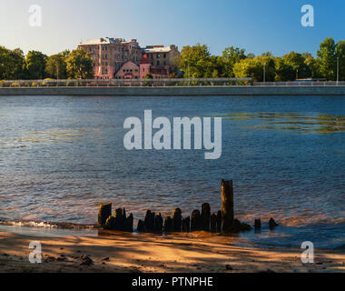 Bahndamm mit historischen Gebäuden und der Bank des Srednyaya Nevka Fluss mit den Resten einer alten hölzernen Pier am Abend im Sommer in St. Pe Stockfoto