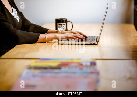 Nahaufnahme der Arme einer Frau, die in einem Büro auf einem Laptop tippt. Stockfoto