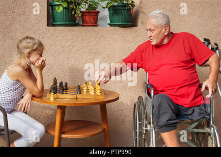 Behinderte Senior und seine schöne junge Enkelin draußen spielen Schach Stockfoto