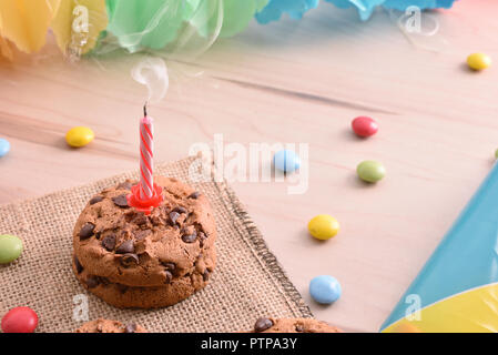 Geburtstag mit erloschen Kerze über Schokolade Cookies auf eine Tabelle mit Süßigkeiten und bunten Bändern. Konzept der Geburtstag. Erhöhte anzeigen. Horizontale co Stockfoto