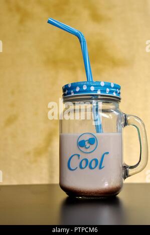 Kakao Milch trinken, in ein großes Glas mit Griff, Blau Deckel und auf gelben Hintergrund Stroh. Im vorderen ist cool und ein emoticon geschrieben. Ansicht von vorn Stockfoto