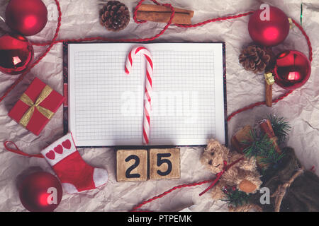 Vorbereitung auf Weihnachten. Weihnachtsdekor auf Papier Oberfläche. Tannenzweigen, rote Kugel, Figuren auf dem Würfel Kalender 25, Spielzeug und Dekor. Top vie Stockfoto