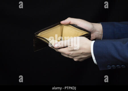 Männliche Geschäftsmann Holding einen leeren Geldbeutel auf ausgestreckten Armen, - und in der Nähe schwarzer Hintergrund Stockfoto