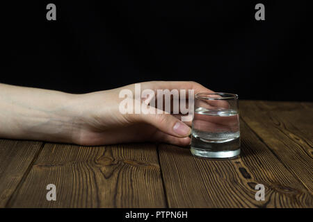 Weibliche hand mit Alkohol in ein Glas auf einer hölzernen Hintergrund, Nahaufnahme, weiblichen Alkoholismus Stockfoto