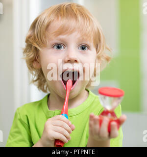 Glückliches Kind Junge Zähne putzen im Badezimmer. Er ist eine dauerhafte Überwachung der Reinigung mit Sanduhr. Stockfoto