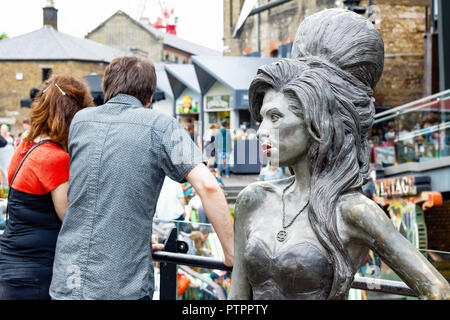 London, Großbritannien - 1 September, 2018 - Bronze Statue des verstorbenen Sängerin Amy Winehouse, von Scott Eaton, im Camden Market mit ein Paar im Hintergrund befindet Stockfoto