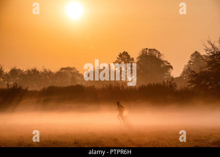 Ein Mann läuft durch den Nebel am frühen Morgen, wenn die Sonne aufgeht über Ackerland in der Nähe der Ortschaft unteren Wraxall in Wiltshire. Stockfoto