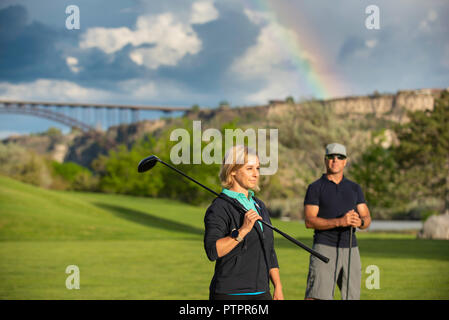 Paar Golfen im Frühjahr mit Regenbogen Overhead. Mann, Frau mit Club über die Schulter nach unten schauen. Der Kurs an der Blauen Seen Country Club Stockfoto
