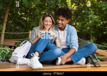Lächelnden jungen multiethnischen Ehepaar miteinander reden, während die Zeit zusammen im Park, mit Handy Stockfoto