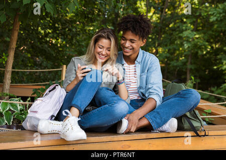 Jungen multiethnischen Ehepaar miteinander reden, während die Zeit zusammen im Park begeistert, mit Handy Stockfoto