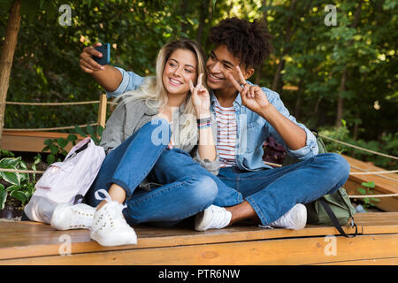 Jungen multiethnischen Ehepaar miteinander reden, während die Zeit zusammen im Park begeistert, wobei ein selfie Stockfoto