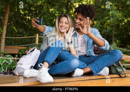 Jungen multiethnischen Ehepaar miteinander reden, während die Zeit zusammen im Park begeistert, wobei ein selfie, winken mit Händen Stockfoto