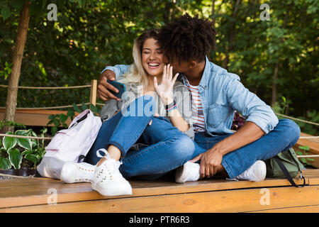 Jungen multiethnischen Ehepaar miteinander reden, während die Zeit zusammen im Park begeistert, wobei ein selfie, küssen Stockfoto