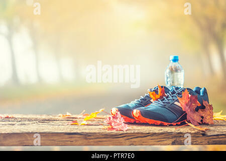 Paar blaue Sport Schuhe und Wasser auf einer Holzplatte in einem Baum Herbst Gasse mit Ahorn Blätter - Zubehör für Übung oder Aktivität Stockfoto
