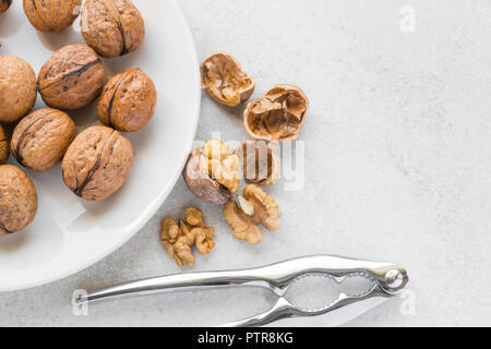 Ganze Walnüsse auf eine weiße Platte, Metall Nussknacker und rissig Walnüsse neben Stockfoto