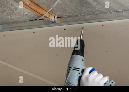 Nahaufnahme der Konstruktor Arbeitnehmer Hand in Schutzhandschuh mit elektrischer Akkuschrauber Anschluss ausgesetzt Trockenbau decke Metallrahmen. Reno Stockfoto