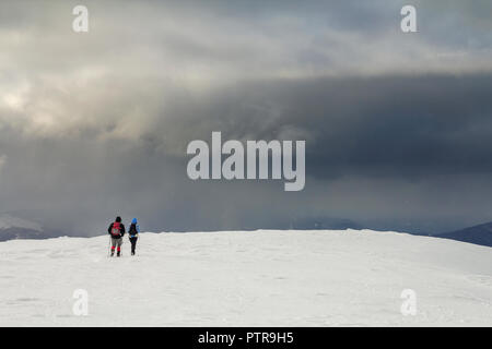 Winter Berglandschaft. Rückansicht des reisenden Touristen Wanderer mit Rucksack auf schneebedeckten Feld und laufen Sie in Richtung des entfernten Berg auf bewölkt dunkel blau St Stockfoto