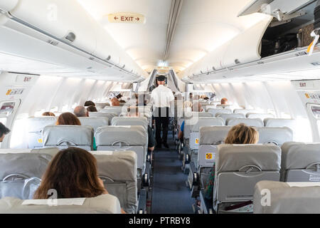 Innenraum der Commercial Airplane mit unkenntlich Passagiere auf ihren Sitzen während des Fluges. Steward in Blau weiße Uniform zu Fuß den Gang der commer Stockfoto