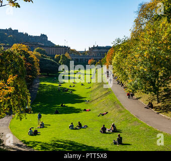 Die Princes Street Gardens, Edinburgh, Schottland, Großbritannien, 10. Oktober 2018. UK Wetter: Menschen sitzen auf der Wiese in der warmen Sonne unter den Herbst Baum Farben Stockfoto