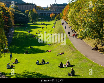 Die Princes Street Gardens, Edinburgh, Schottland, Großbritannien, 10. Oktober 2018. UK Wetter: Menschen sitzen auf der Wiese in der warmen Sonne unter den Herbst Baum Farben Stockfoto