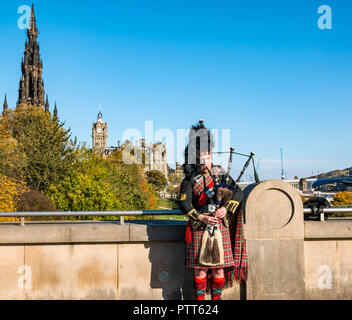 The Mound, Edinburgh, Schottland, Großbritannien, 10. Oktober 2018. Wetter in Großbritannien: Ein Dudelsack-Dudelsackspieler im warmen Sonnenschein unter den Herbstbaumfarben mit dem Turm des Scott-Denkmals und dem Uhrenturm des Balmoral Hotels im Hintergrund Stockfoto