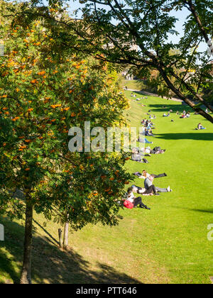 Princes Street Gardens, Edinburgh, Schottland, Großbritannien, 10. Oktober 2018. UK Wetter: Menschen sitzen auf dem Gras in der unerwartet warmen Sonnenschein zwischen den Herbstbaumfarben und blühenden Rowan Pomes oder Beeren Stockfoto