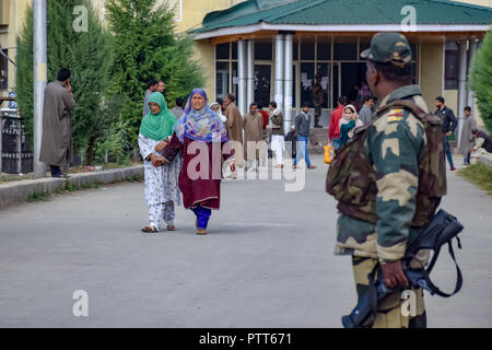 Oktober 10, 2018 - Baramulla, Jammu und Kaschmir, Indien - Eine Armee Mann gesehen stehen auf der Hut wie Frauen gehen Sie von einem Wahllokal während der Wahlen.. Zweite Phase der städtischen lokalen Körper (ULB) Wahlen in Jammu und Kaschmir. Sommer Hauptstadt des Indischen kontrollierten Kashmir, Srinagar. Dieser hatte den niedrigsten Umsatz der Wähler bei den Kommunalwahlen. (Bild: © idrees Abbas/SOPA Bilder über ZUMA Draht) Stockfoto