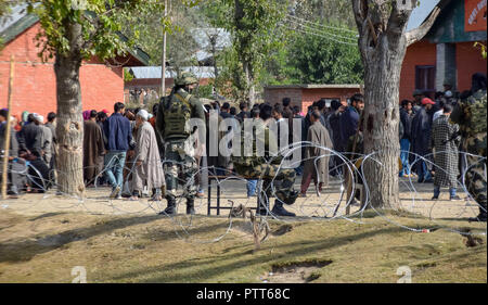 Oktober 10, 2018 - Baramulla, Jammu und Kaschmir, Indien - Eine Armee Mann gesehen auf der Suche als Kaschmir Wähler in eine Warteschlange außerhalb der Wahllokale während der Wahlen im Bereich der Distrikt Baramulla sumbal warten.. Zweite Phase der städtischen lokalen Körper (ULB) Wahlen in Jammu und Kaschmir. Sommer Hauptstadt des Indischen kontrollierten Kashmir, Srinagar. Dieser hatte den niedrigsten Umsatz der Wähler bei den Kommunalwahlen. (Bild: © idrees Abbas/SOPA Bilder über ZUMA Draht) Stockfoto