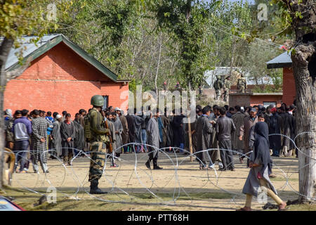 Oktober 10, 2018 - Baramulla, Jammu und Kaschmir, Indien - Eine Armee Mann gesehen auf der Suche als Kaschmir Wähler in eine Warteschlange außerhalb der Wahllokale während der Wahlen im Bereich der Distrikt Baramulla sumbal warten.. Zweite Phase der städtischen lokalen Körper (ULB) Wahlen in Jammu und Kaschmir. Sommer Hauptstadt des Indischen kontrollierten Kashmir, Srinagar. Dieser hatte den niedrigsten Umsatz der Wähler bei den Kommunalwahlen. (Bild: © idrees Abbas/SOPA Bilder über ZUMA Draht) Stockfoto