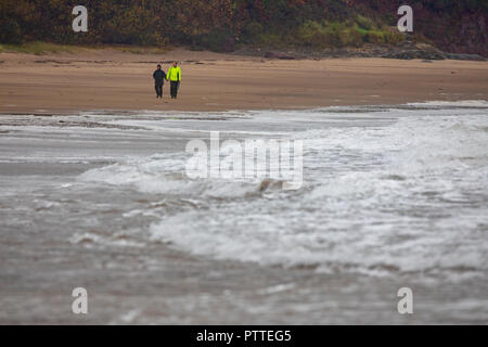 Süßwasser-Ost, Pembrokeshire, Wales, 11 Uhr Oktober 2018. UK Wetter: Nass stürmisches Wetter beginnt für schwere See mit Sturm Callum bilden für eine stürmische Wochenende voran Pembrokeshire, Wales zu machen. Ein paar Mutige die nassen und windigen Wetter für einen Spaziergang entlang der Küste, wie Wellen in das Ufer, Süßwasser-Ost, Pembrokeshire © DGDImages/AlamyNews Stockfoto