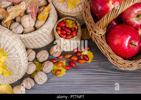 Walnüsse, rote Äpfel im Korb, Hagebutten und gelbe Blätter auf einer hölzernen Oberfläche, gesunde Nahrung aus der Natur. Konzept der Herbst Hintergrund Stockfoto