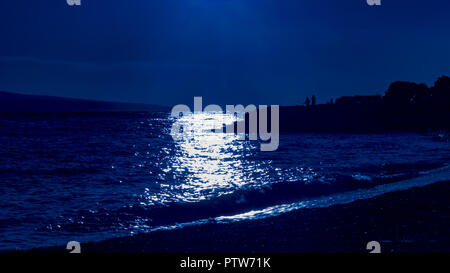 Sonnenuntergang über dem Meer in Blau. Silhouette von Strand und Hafen mit Fischer. Stockfoto