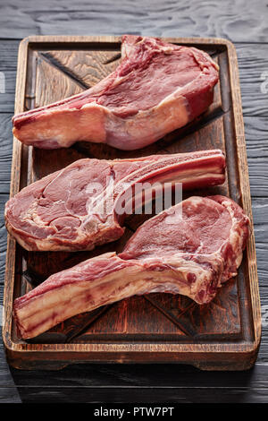 Drei trockenen Jahren Roh tomahawk Rindersteaks auf einem alten unfreundlich Holz Schneidebrett, close-up Stockfoto