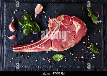 Trocken im Alter von raw Tomahawk oder Cowboy Rindersteak auf einer Steintafel mit Gewürzen, Pfeffer, Knoblauch und Basilikum, Nahaufnahme, Flach, Ansicht von oben Stockfoto