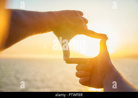 Die Hände des Menschen Ausdehnung in Richtung der Sonne auf dem Meer. Ein Mann sieht den Sonnenuntergang durch die eingeklappte Finger Stockfoto