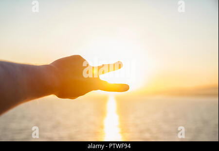 Die Hände des Menschen Ausdehnung in Richtung der Sonne auf dem Meer. Ein Mann sieht den Sonnenuntergang durch die Gefalteten Fingern. Stockfoto