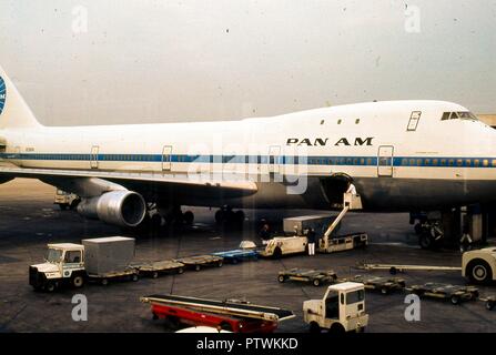 Portrait der "Clipper Victor", ein Pan American World Airways 747 Jet Flugzeug am Terminal Gate am Flughafen Heathrow geparkt, außerhalb von London, England, November, 1973. Gepäckabfertigung warten mit ihren Leerlauf Gepäckträger Lkw unter dem Flugzeug öffnen Laderaum Tür. Diese bestimmten Luftfahrzeug, einem Boening 747-121 mit der Registrierungsnummer N 736 PA, hat eine berüchtigte doppelte Auszeichnung: Er bedient den Eröffnungs-Pan Am kommerziellen 747 Jet Flug am 22. Januar 1970, und sieben Jahre später wurde im Flughafen Teneriffa Disaster" vom 27. März 1977, die tödlichste Unfall in der Geschichte der Luftfahrt zerstört Stockfoto
