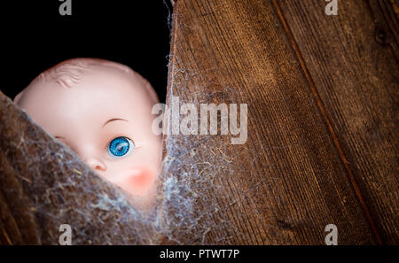 Alte Kunststoff Puppe mit hellen blauen Augen blickt durch ein Cob web Klappe abgedeckt. Stockfoto