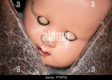 Alte Kunststoff Puppe mit geschlossenen Augen blickt durch ein Cob web Klappe abgedeckt. Stockfoto