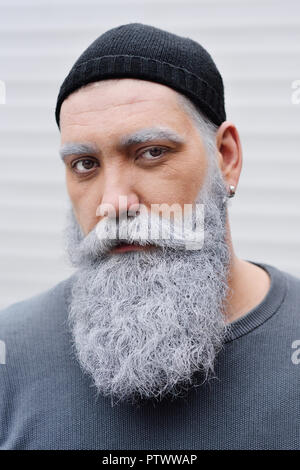 Attraktive Mann mittleren Alters mit einem großen grauen Bart in eine Kappe in die Kamera schaut Stockfoto